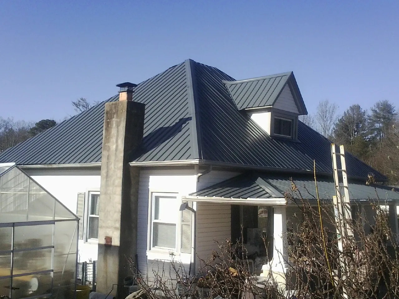 Dark blue standing seam metal roof on a white farmhouse with dormer — Slate & Tile Roof Repair by Roofing Brothers in Maynard