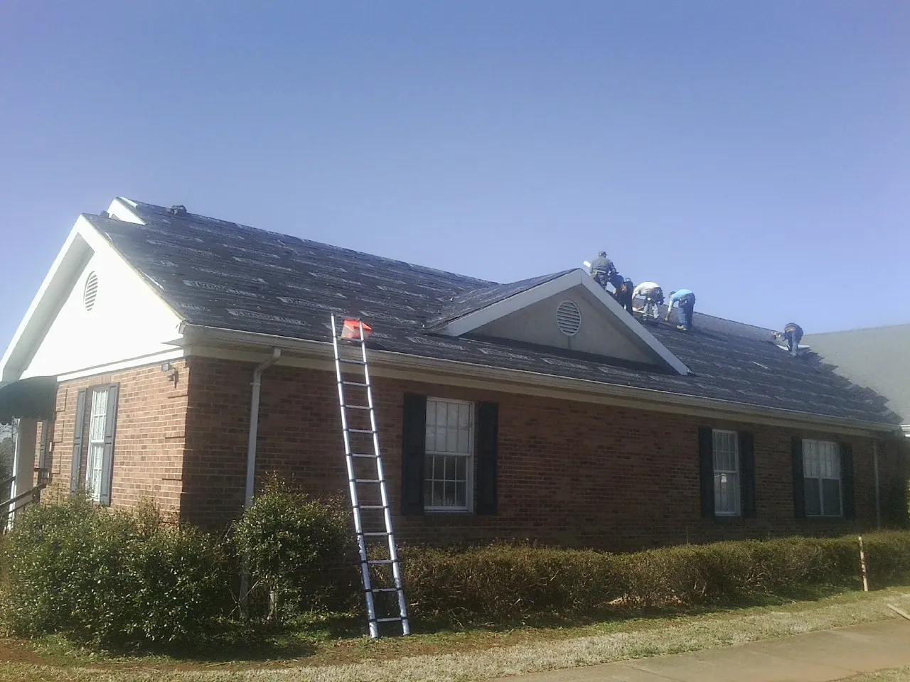 Crew tearing shingles off a brick ranch roof with a ladder set — Emergency Roof Repair work by our crew in Maynard