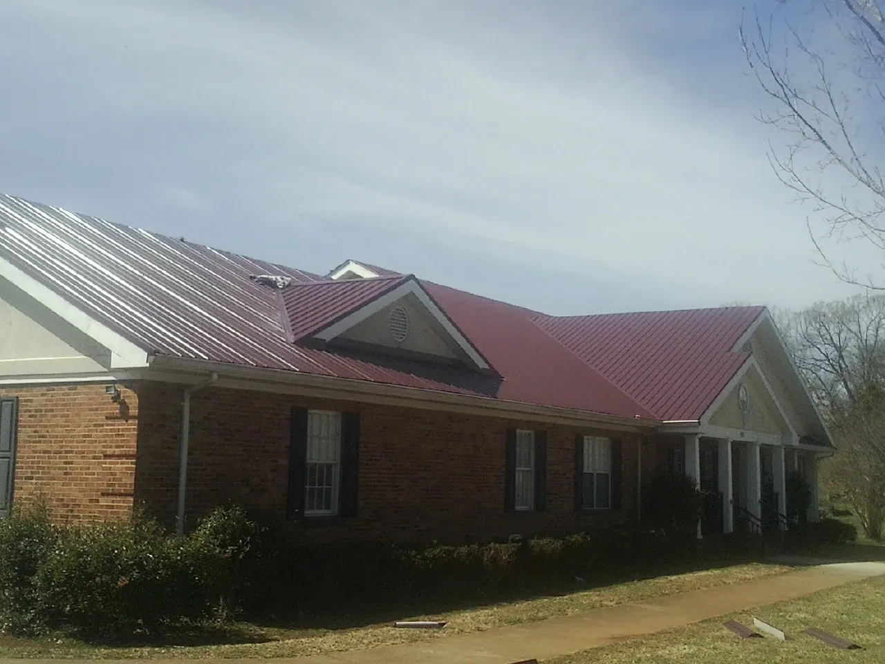 Red metal roof with gabled entries on a long brick building, from a Hail Damage Roof Repair job in Maynard